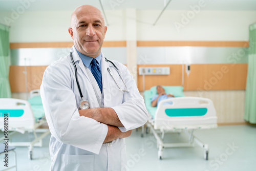 Portrait of Caucasian doctor stand with confidence action and smile stay in front of patient on bed in healthcare room.