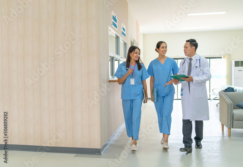 Doctor and nurse discuss together about diagnosis and treatment work during walk in the way in hospital near reception counter.