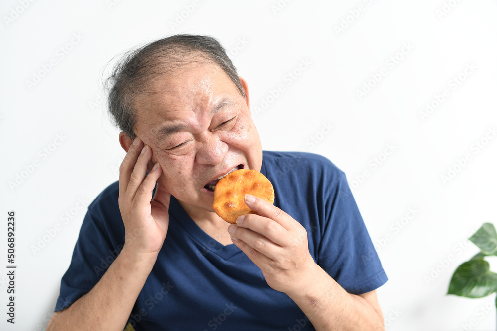 辛い表情で煎餅を食べる高齢者の男性