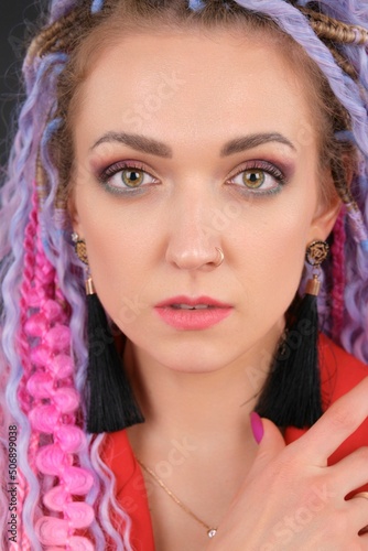 Close-up face portrait of original style young woman who has colorful hair  afro braids dreads. She looks at camera. Concept of creativity  modern people  youngsters with informal style