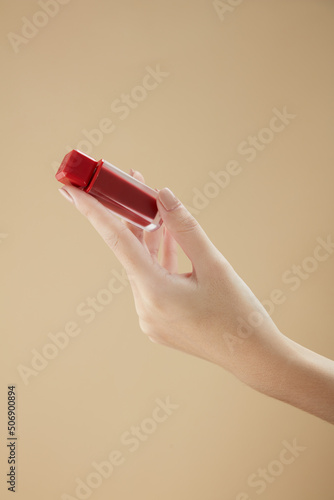 Top view of hand model using lipstick on hand in beige background for cosmetic advertising