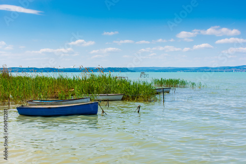 Fishing boats are moored to the shore of a lake with turquoise water.
