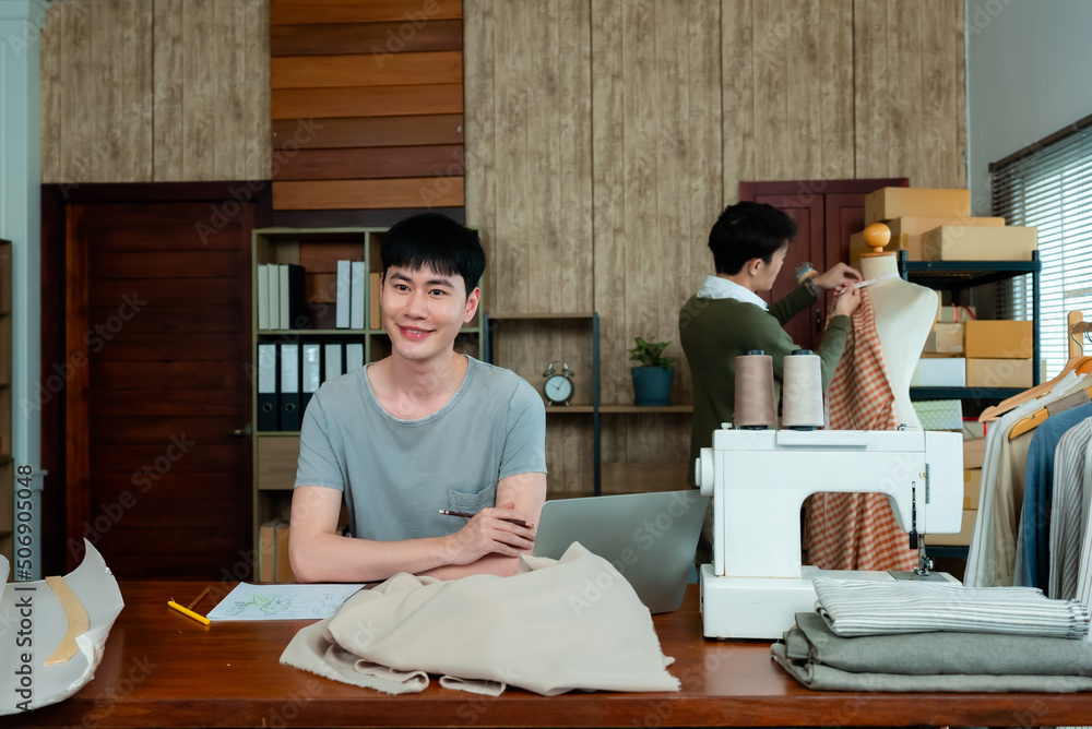 Young LGBTQ Asian Men Small Business Partner,The artist is designing the clothes, and there is an assistant standing and holding the cloth, Professional Design clothes to sell online. Young LGBTQ Asian Men Small Business Partner,The artist is designing the clothes, and there is an assistant standing and holding the cloth, Professional Design clothes to sell online.