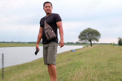 An Indonesian young man standing by the lake with a sling bag over his shoulder photo