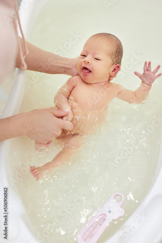 Fototapeta mother bathes her baby in a white small plastic tub