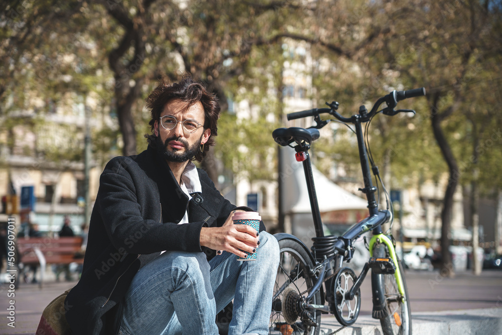 Fototapeta premium Young man sitting on the bench holding cup of coffee