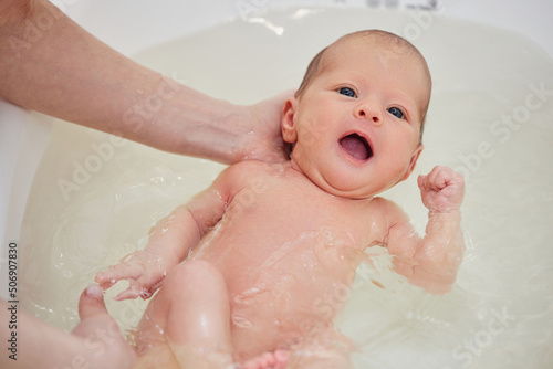 Fotografie mother bathes her baby in a white small plastic tub
