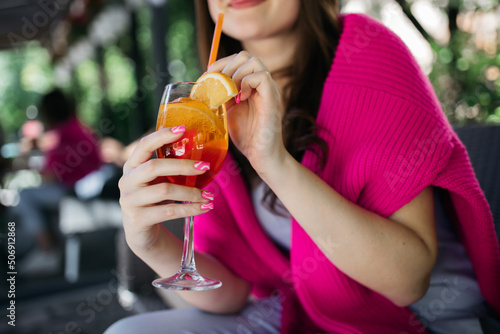 Young girl holding an aperol spritz. Cocktail aperol spritz in a glass. Young girl in a restaurant with a glass. Aperol spritz in the hands of a girl. Aperol spritz. Cocktail.