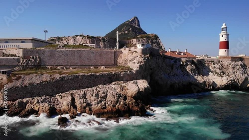 Waves from the swell of the Mediterranean splash on the cliffs below the lighthouse against the background of the great Muslim mosque and the upper rock of Gibraltar Close up drone lifted panning shot