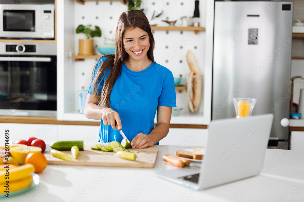 Young woman reading online recipes while cutting vegetable for salad in the kitchen