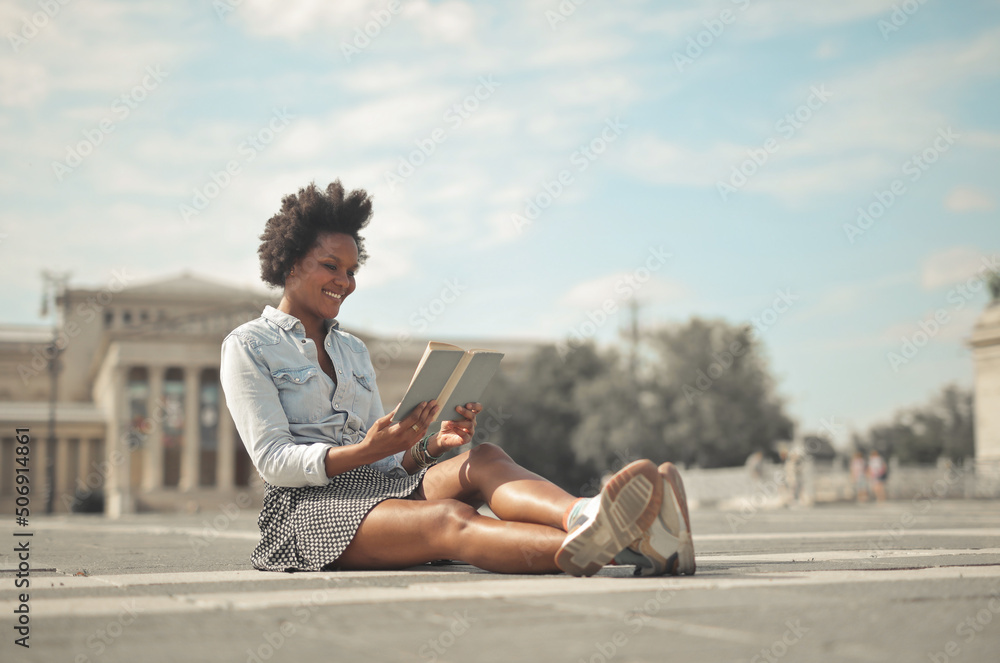 happy woman is reading a book sitting on the street