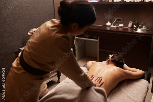 Slika na platnu Rear view of a masseuse gives a body massage to a young woman