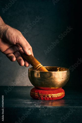 a hand with a hammer and a Tibetan bowl on a dark background