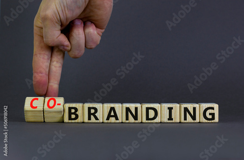 Branding or co-branding symbol. Businessman turns wooden cubes and changes the word Branding to Co-branding. Beautiful grey table grey background, copy space. Business branding co-branding concept.