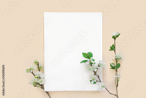 Blank greeting card, invitation mockup. Apple flowers, blossoming plant on beige table background. Flat lay, top view. Copyspace. Canvas mock up. Modern Minimal business brand template. Soft shadow