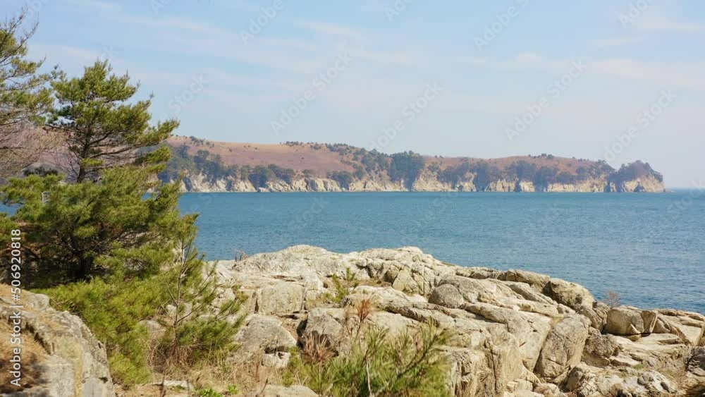 View from a drone moving through the trees over the calm blue surface of clear sea water. Beautiful rocks covered with coniferous trees. Weekend vacation concept. View from a drone moving through the trees over the calm blue surface of clear sea water. Beautiful rocks covered with coniferous trees. Weekend vacation concept.