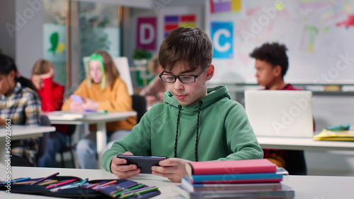 Teenage boy watching video on smartphone sitting at desk in class