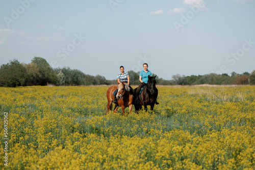 Two female riders on horseback standing on blooming meadow.