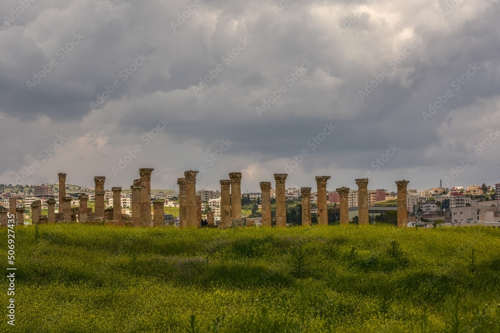 Ancient Corinthian Columns in the Roman city of Jerash in Jordan with a cloudy sky and a green meadow