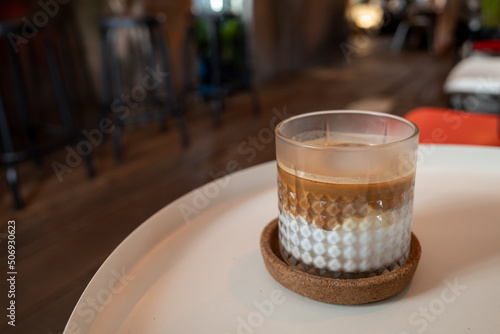 Transparent Glass Cup of latte, flat white or piccolo coffee on white coffee table and blur interior cafe. photo