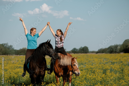 Two happy woman on horseback holding hands and looking at each other in outdoors.