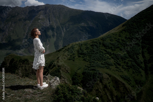 Slim brunette girl in a white dress is walking in the mountains. © Alex