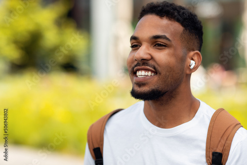 Happy young man listening to music in earbuds walking outdoors