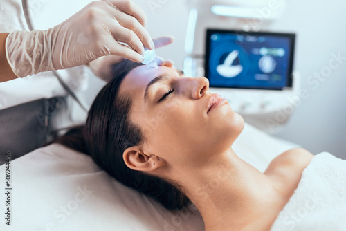 Cosmetologist making ultrasonic cleaning and rejuvenation the face to beautiful woman on the spa center.