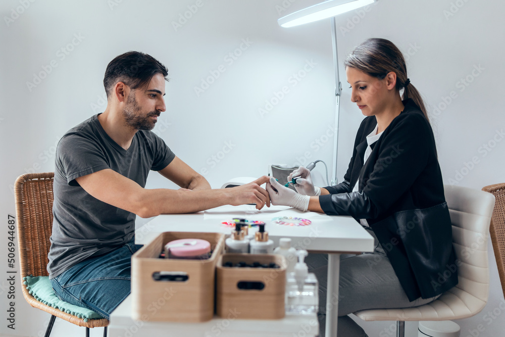 Fototapeta premium Cosmetologist woman making permanent manicure to handsome man in salon. Beauty concept.