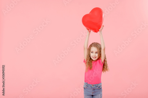Adorable little girl holding red balloon heart shaped on pink background. Mother's day, valentine's day, love, feeling, family concept.