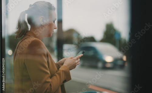Woman with smartphone is waiting for bus at bus stop.