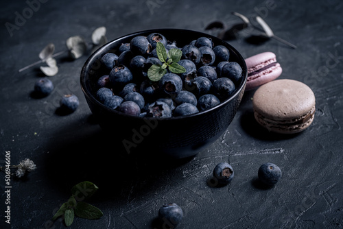 close-up of fresh blueberries in a black bowl with macaroons around on a black slate. the macaroon a small French almond cake. close-up view