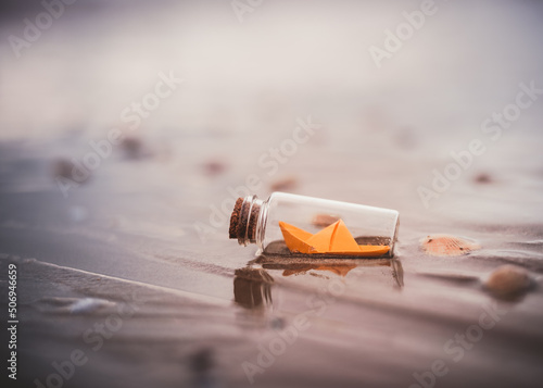 Miniature origami ship in bottle standing on sand at sunrise