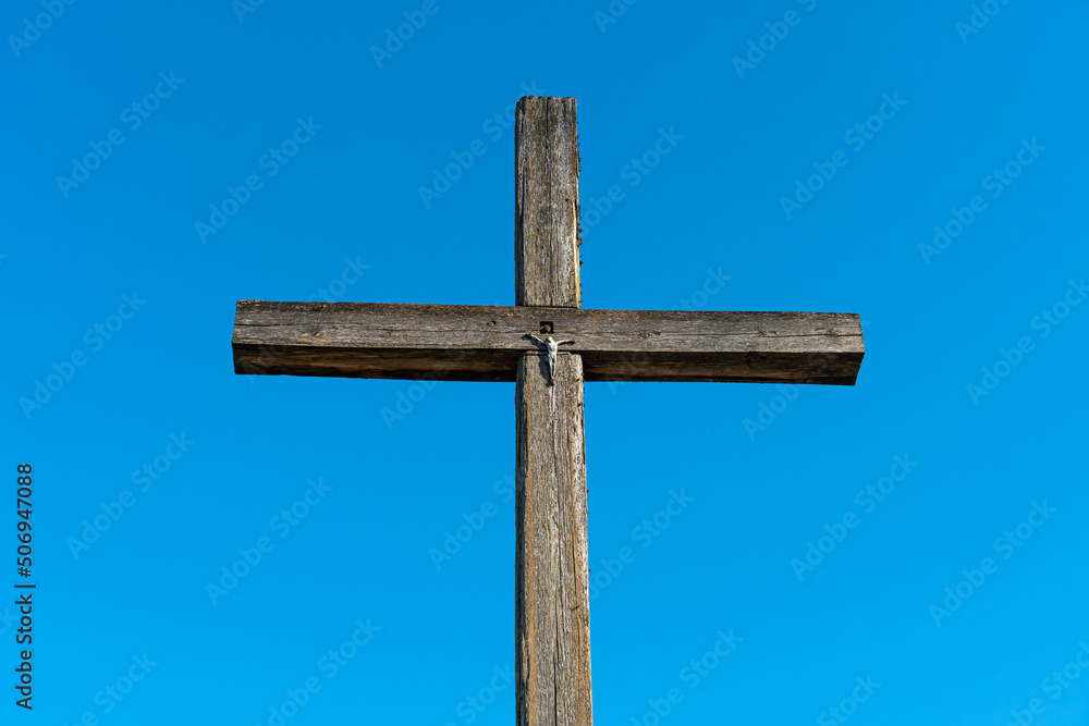 An old wooden cross against a clear blue sky. The crucified Jesus on the cross. The concept of the pure and unrequited love of God Jesus Christ for man. An old wooden cross against a clear blue sky. The crucified Jesus on the cross. The concept of the pure and unrequited love of God Jesus Christ for man.