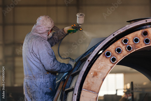 Foto Painter worker with sprayer painting machine part in factory workshop