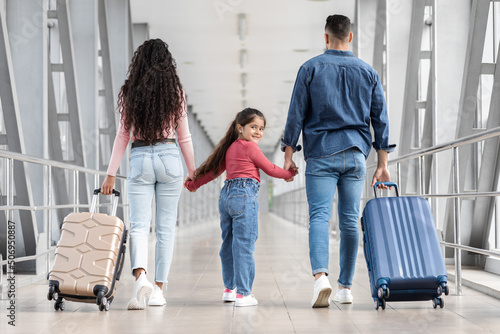 Little girl going on holiday with parents, walking with suitcases at airport