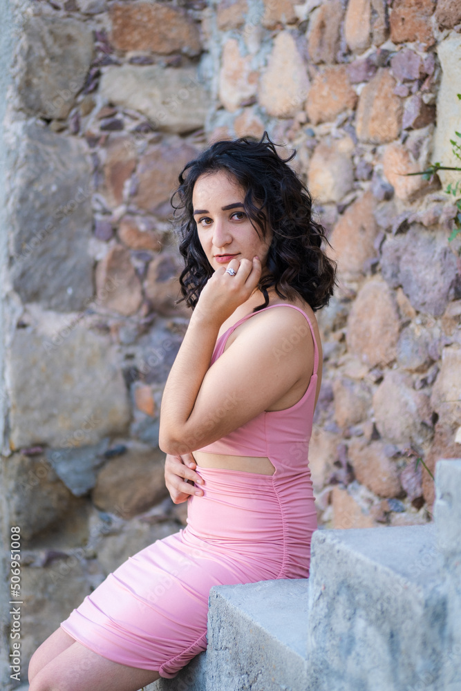Pretty dark haired woman posing in short pink dress in urban eviroments