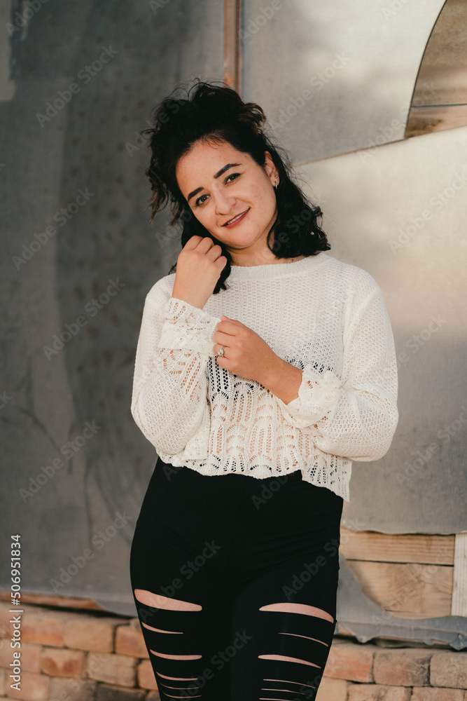Fototapeta premium Dark haired woman poses in white knit top in front of broken mirror