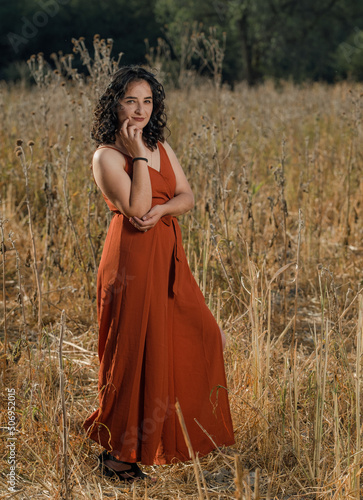 Pretty Latina posing in orange dress in an autumn field