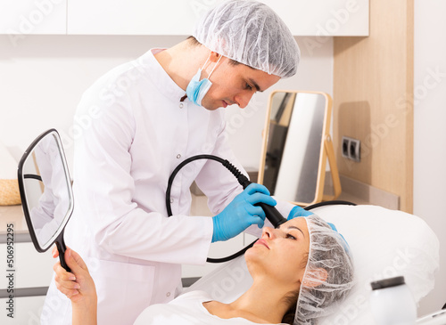 Obraz na plátně Experienced male beautician performing female face skin rf lifting procedure on