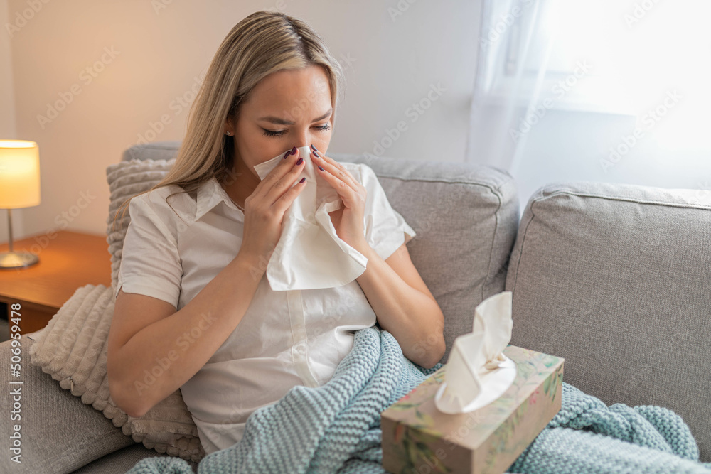 Sick woman sitting under the blanket. Sick woman with seasonal infections, flu, allergy lying in bed. Sick woman covered with a blanket lying in bed with high fever and a flu, resting and drinking tea Sick woman sitting under the blanket. Sick woman with seasonal infections, flu, allergy lying in bed. Sick woman covered with a blanket lying in bed with high fever and a flu, resting and drinking tea