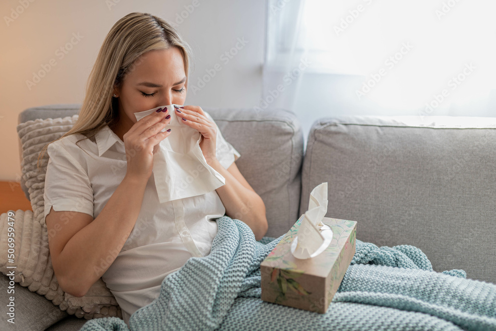 Sick woman sitting under the blanket. Sick woman with seasonal infections, flu, allergy lying in bed. Sick woman covered with a blanket lying in bed with high fever and a flu, resting and drinking tea Sick woman sitting under the blanket. Sick woman with seasonal infections, flu, allergy lying in bed. Sick woman covered with a blanket lying in bed with high fever and a flu, resting and drinking tea
