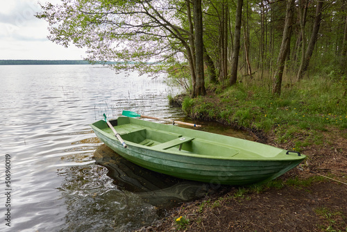 Small green boat anchored in forest lake. Scandinavia. Transportation, traditional craft, recreation, leisure activity, healthy lifestyle, local tourism, sport, rowing, hiking, summer vacations themes photo