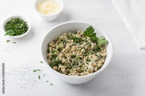 Pearl barley with cheese and herbs in white ceramic bowl on a light gray background, top view. Delicious and healthy breakfast