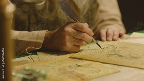 Old man with beard dressed like Leonardo Da Vinci writing , painting and working in vintage 15 - 16 century designed room . Big drawing of famous artwork  . Dipping ink pen on inkwell . Slow motion 