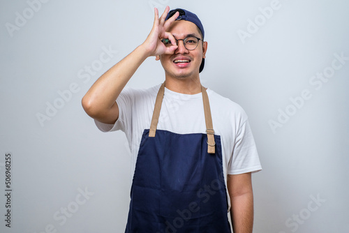 Young handsome barista man wearing apron smiling and doing ok sign with fingers, excellent symbol