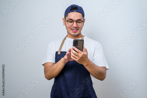 Young man barista man wearing apron work in coffee shop using mobile cell phone chat and smiling