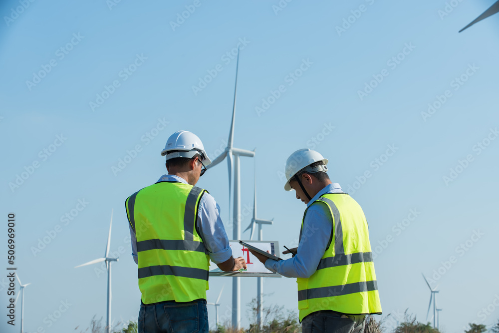 Back view of two engineers discussing against turbines on wind turbine farm. Back view of two engineers discussing against turbines on wind turbine farm.