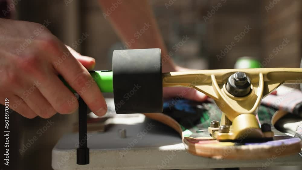 Man's hands as he uses tool to unscrew longboard wheel. Man's hands as he uses tool to unscrew longboard wheel.