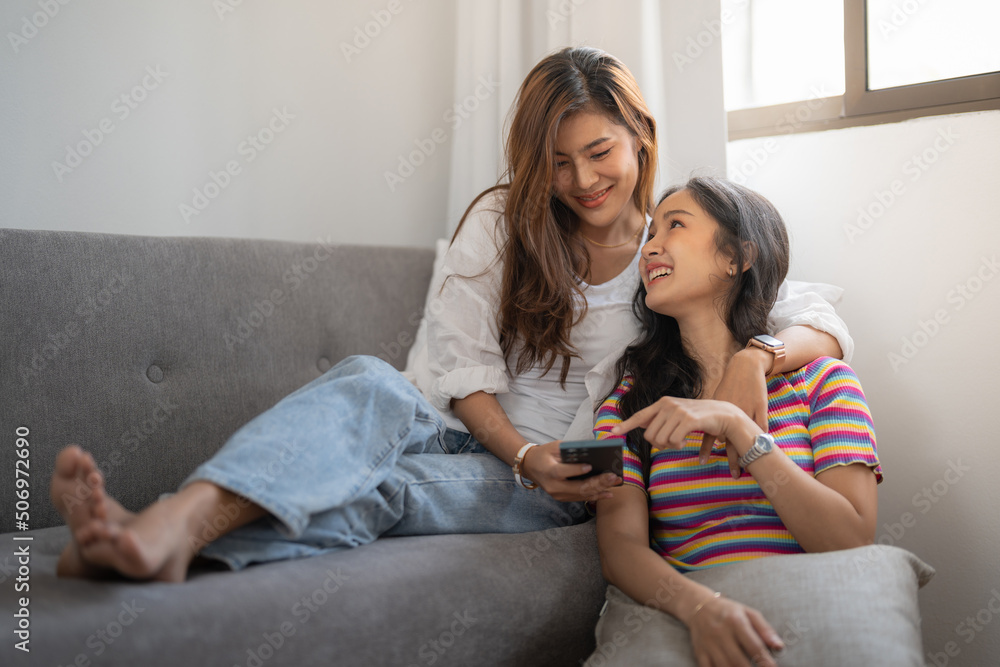 Two happy young asian casual women having fun using smartphone at home. Lesbian millennial couple concept. Two happy young asian casual women having fun using smartphone at home. Lesbian millennial couple concept.